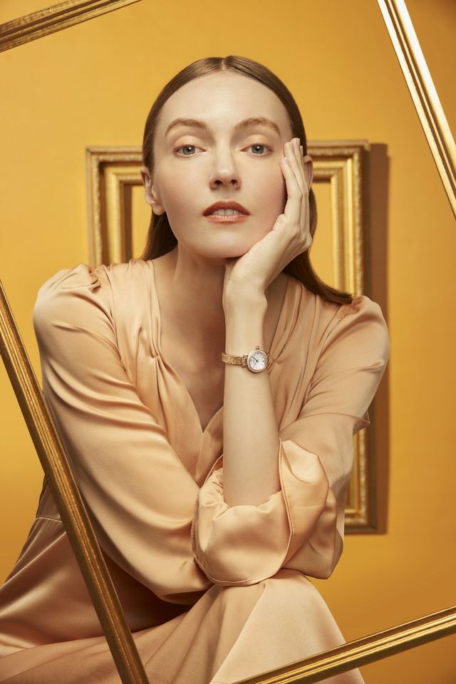 Modelo con un reloj de esfera clara sobre fondo dorado